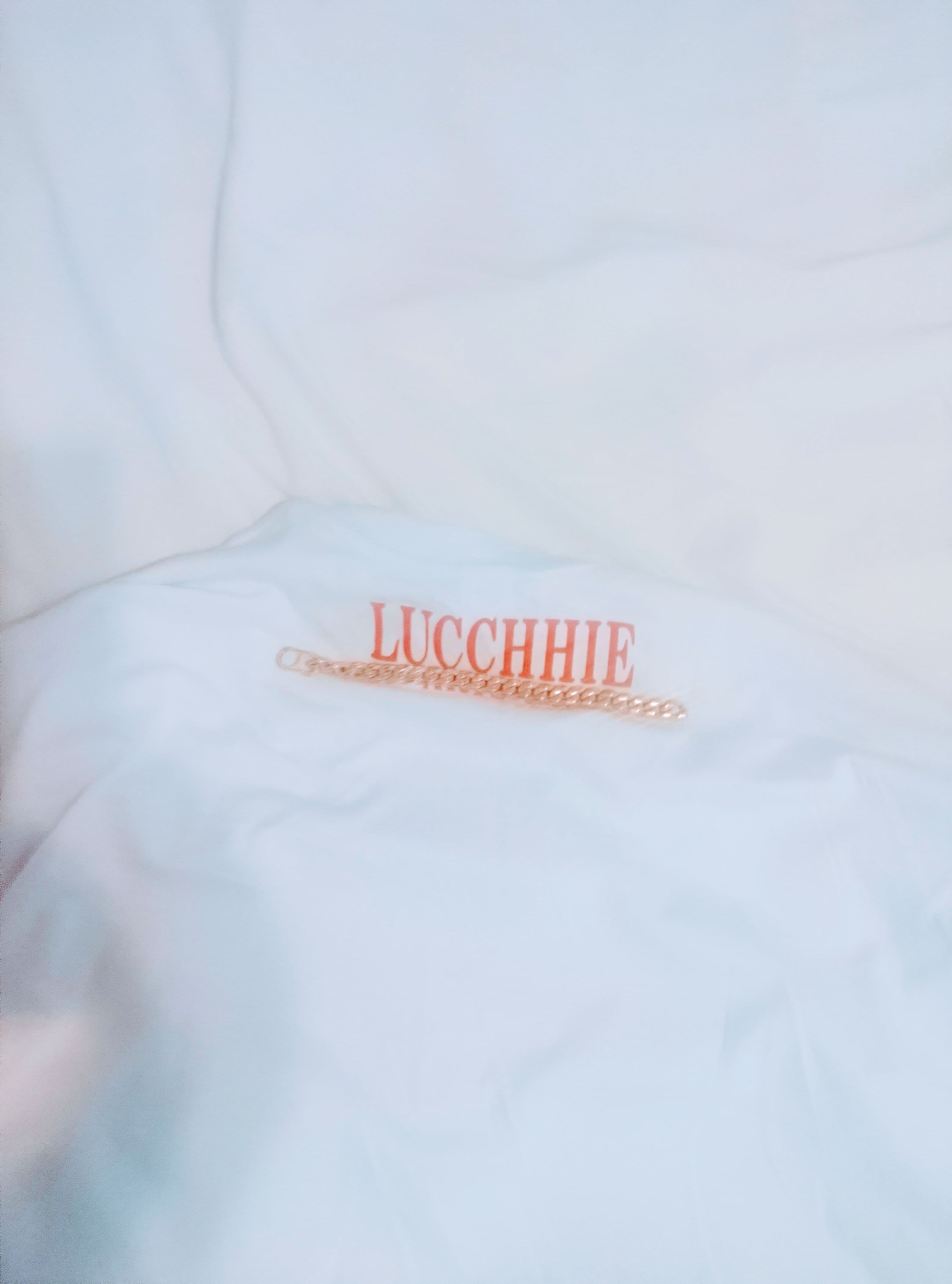 Bracelet en chaîne dorée sur un tissu blanc portant le nom LUCCHHIE en rouge.